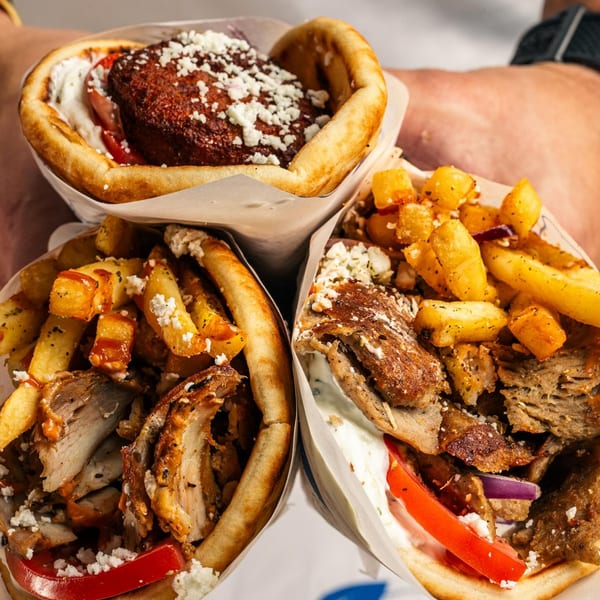 Three delicious gyros with meat, fries, tomatoes, and feta cheese, held by a person.