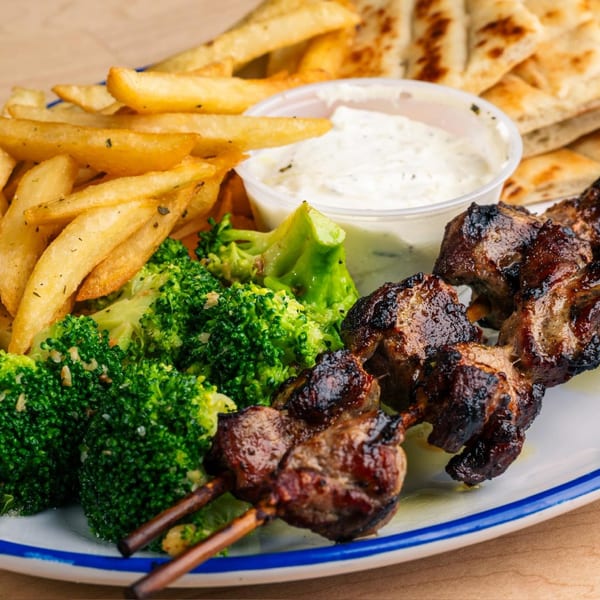 Grilled meat skewers with fries, broccoli, tzatziki sauce, and pita bread on a white plate.
