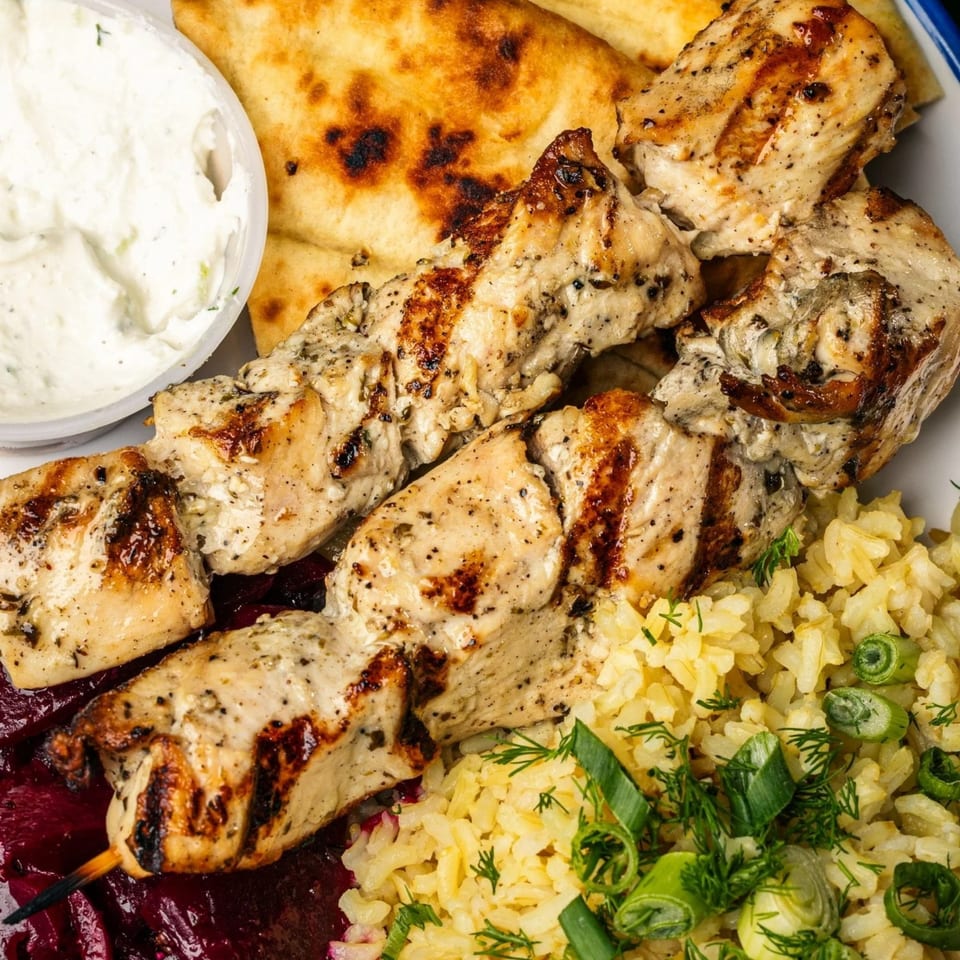 Grilled chicken skewers with rice, red cabbage, pita bread, and a side of tzatziki sauce.