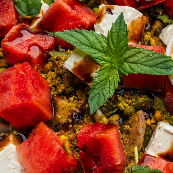 Close-up of watermelon, feta, pistachios, mint, and balsamic glaze, creating a vibrant salad.