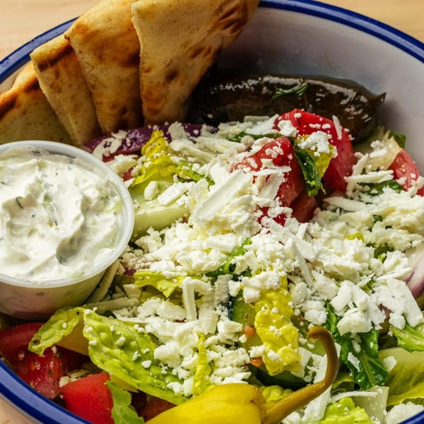 A Greek salad with feta, tomatoes, lettuce, pita bread, dolmades, and tzatziki sauce.