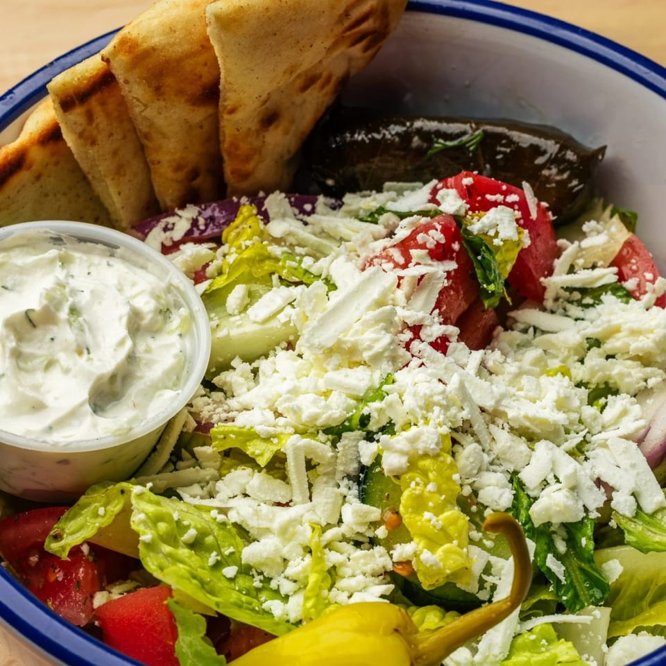 A Greek salad with feta, tomatoes, lettuce, pita bread, dolmades, and tzatziki sauce.