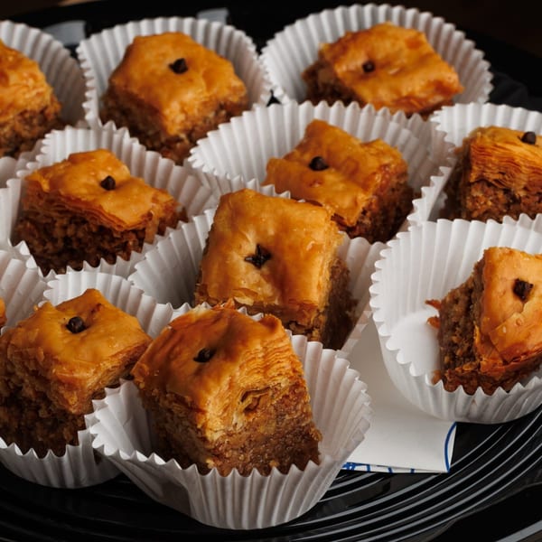 A close-up of several individual baklava pastries in white paper cups on a black tray.