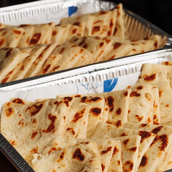 Two foil trays filled with rows of golden-brown pita bread triangles, ready for serving.
