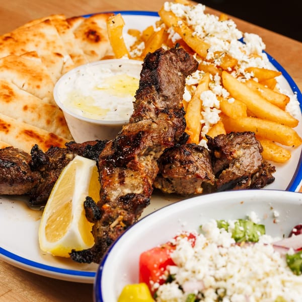 Grilled meat skewers with pita bread, tzatziki, feta fries, and a side salad.